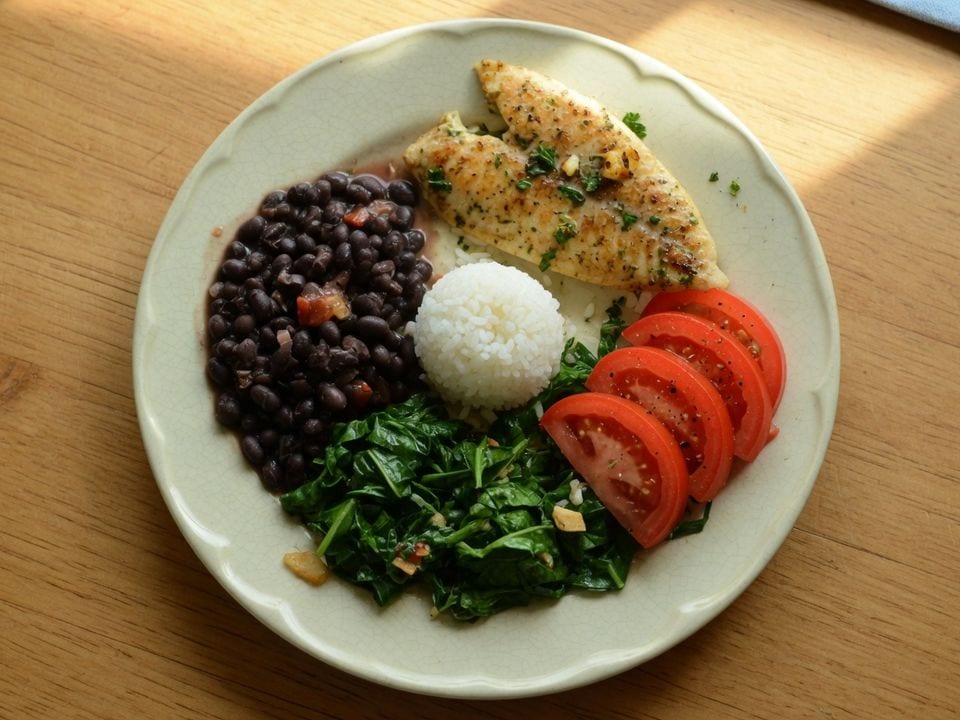 Prato com peixe, arroz, feijão-preto, couve e tomate.